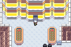 The player at the door of the yellow-striped Battle Factory, two flower beds on the plaza below
